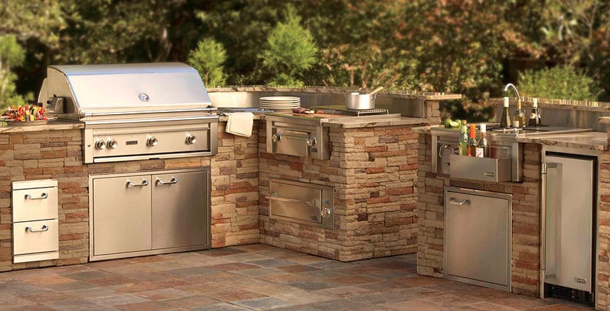 Outdoor kitchen with BBQ pit, mini fridge, stove top, faucet and more.