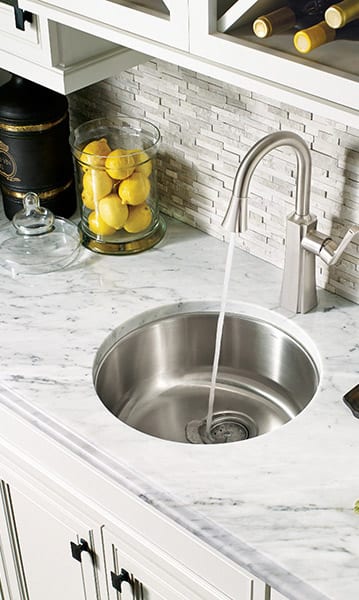 Circular faucet design with marble counters and gray tile back splash