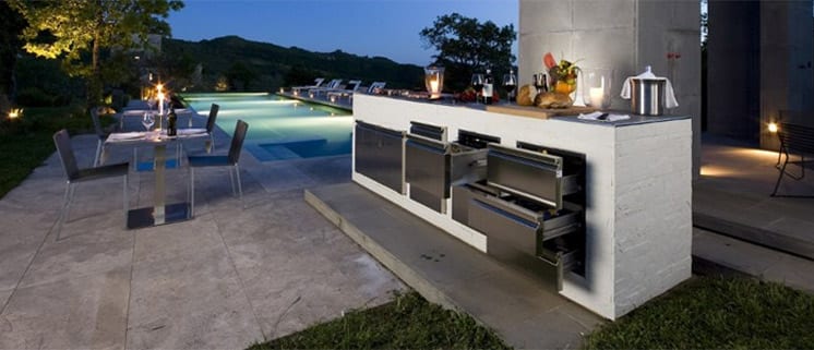 Beautiful outdoor kitchen with candle lit table and beautiful pool in the background.